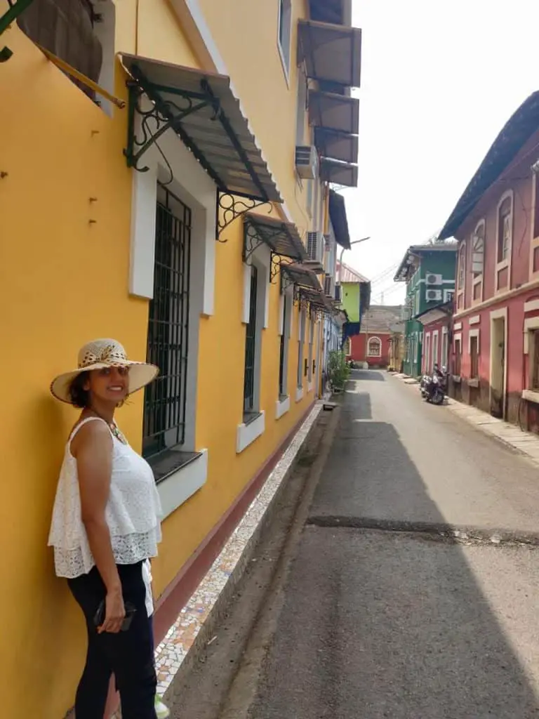 A picture of me walking down the Fontainhas lane donning a white sleeveless top with a black denim. A chic Goa trip outfit for women, especially during hot weather.