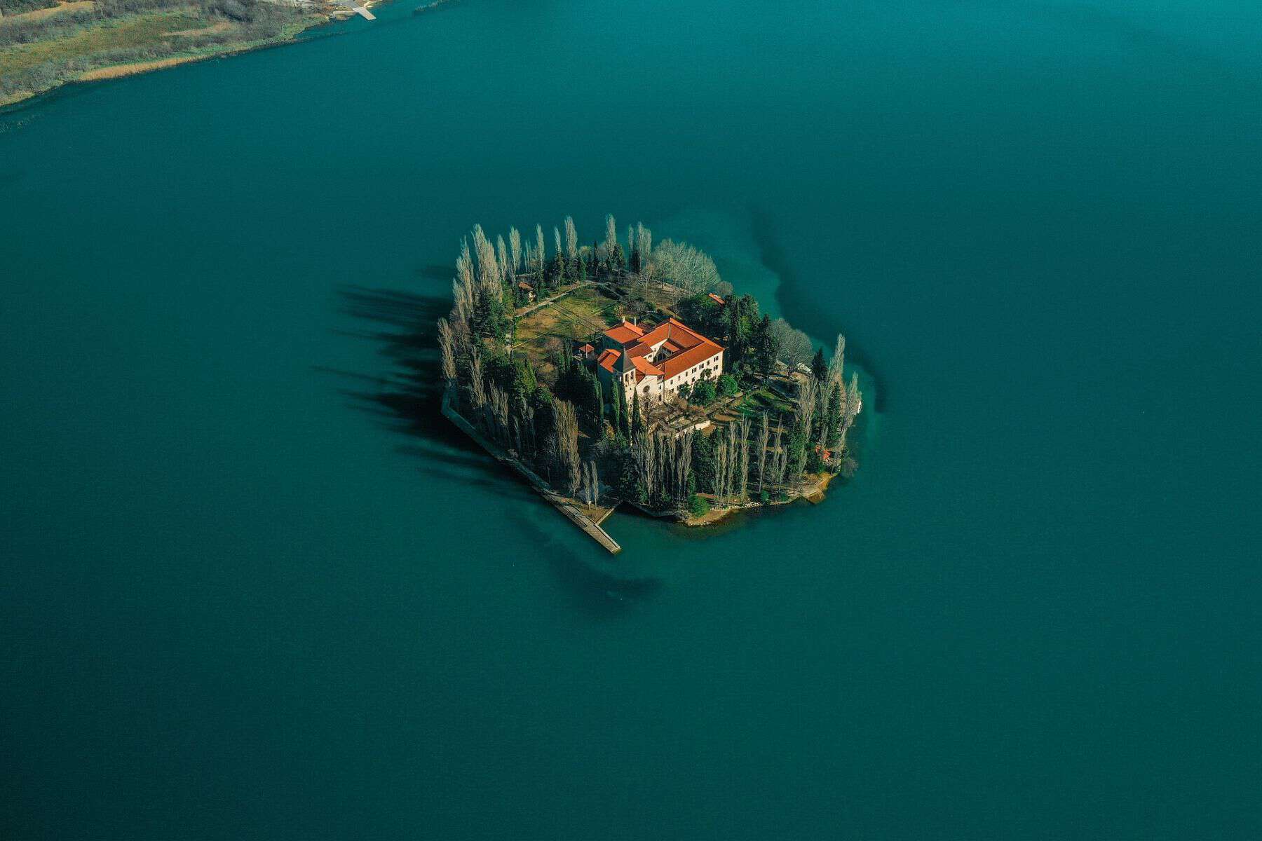 An aerial view of a small, tree-lined island in Croatia, featuring a red-roofed building surrounded by dense greenery, sitting in the middle of a serene turquoise lake.
Choose the best Croatia Quote for Instagram to go along with this image