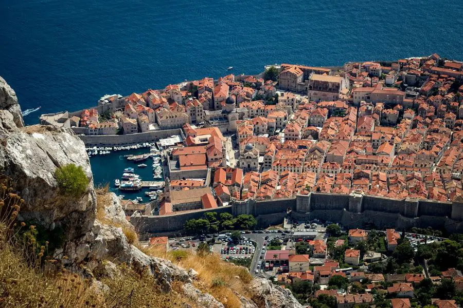 A breathtaking aerial shot of Dubrovnik, Croatia, showcasing the historic walled city with its iconic terracotta rooftops and a bustling marina next to the deep blue Adriatic Sea. 