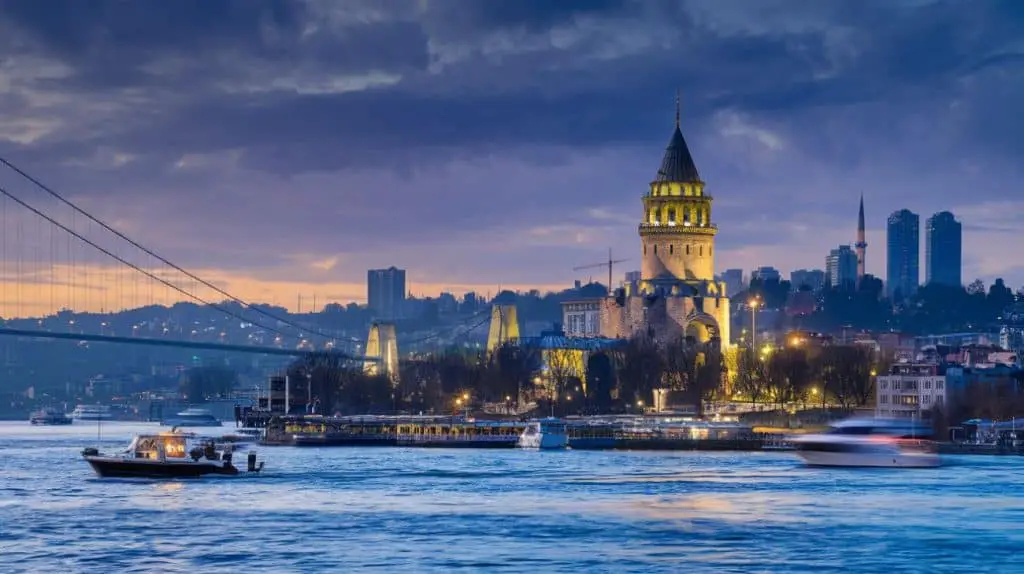 A serene view of the Bosphorus Strait in Istanbul during sunset, with boats gliding on the water, a suspension bridge in the distance, and city buildings on both sides of the strait—perfect for Istanbul Instagram captions and quotes.