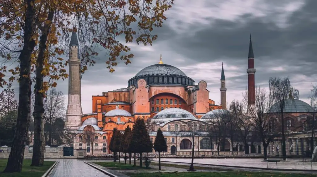 A majestic view of the Hagia Sophia with its iconic domes and minarets framed by autumn trees under a dramatic cloudy sky, showcasing Istanbul's rich cultural heritage—ideal for Istanbul Instagram captions and quotes.