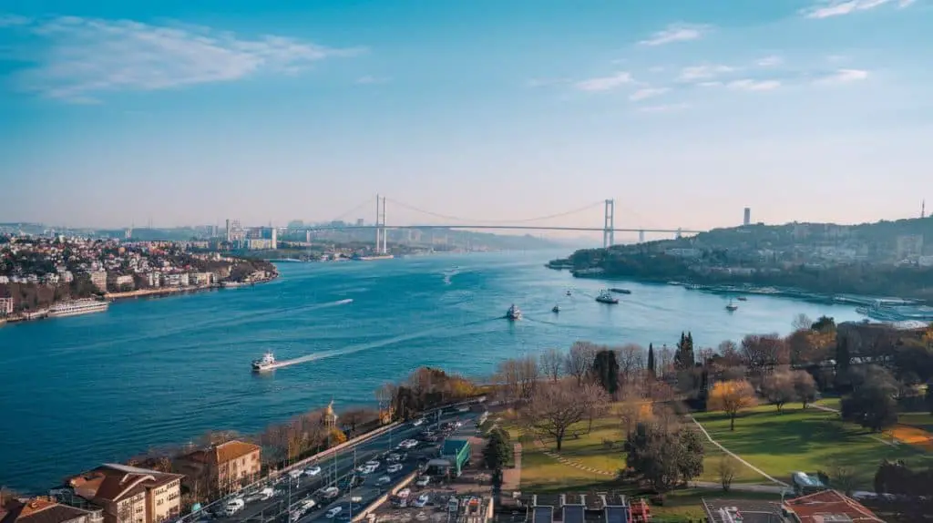 A breathtaking view of the Bosphorus in Istanbul at sunset, featuring ferries and boats moving along the water, modern skyscrapers and historic mosques on the shoreline, and a suspension bridge connecting the continents—a stunning scene for Istanbul Instagram captions and quotes about the city's timeless charm.