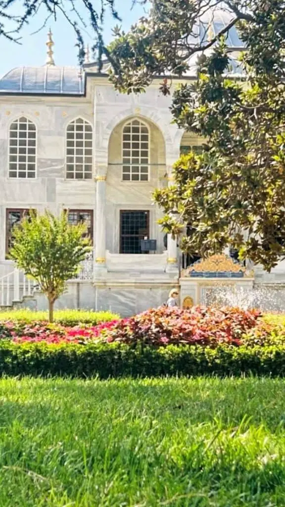  A serene garden in Istanbul with neatly trimmed hedges and vibrant flowers in front of a historical Ottoman-style building, a picturesque shot for an Istanbul Instagram story.