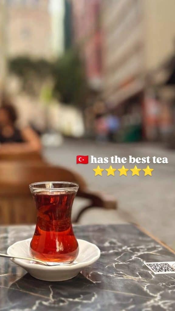 A steaming cup of Turkish tea on a marble table, with a blurred street view in the background and text praising Turkey's tea culture. An ideal food highlight for an Istanbul Instagram story.