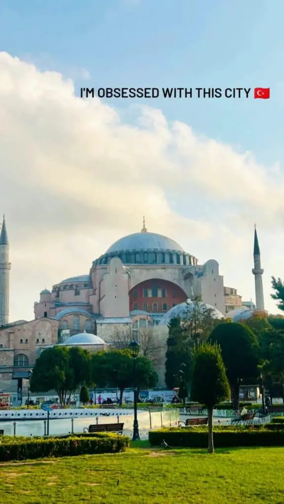 The iconic Hagia Sophia in Istanbul, framed by a clear blue sky and lush green park grounds, stands as a symbol of history and culture. The text overlay reads, "I'm obsessed with this city" with a Turkish flag emoji, highlighting the charm of Istanbul for an Instagram story