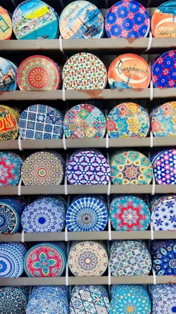 A collection of vibrant and intricately patterned coasters or ceramic plates displayed on shelves, featuring Ottoman and Turkish designs.

