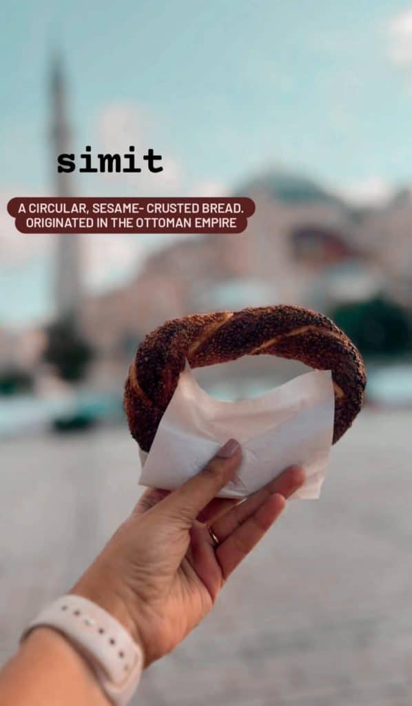 A hand holding a freshly baked simit (a circular, sesame-crusted bread), with a blurred background showing the silhouette of a mosque and text overlay describing simit as “A circular, sesame-crusted bread. Originated in the Ottoman Empire,” highlighted in an Istanbul Instagram story.