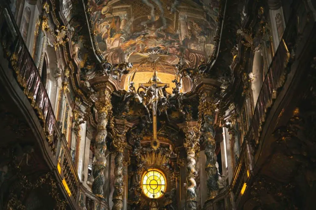 The stunning interior of Asam Church in Munich, Germany, showcasing intricate Baroque architecture with golden sculptures, towering marble columns, and a dramatic fresco-covered ceiling. This hidden gem is a must-visit for travelers exploring the best "Things to do in Munich," offering a glimpse into the city's rich artistic and religious history.