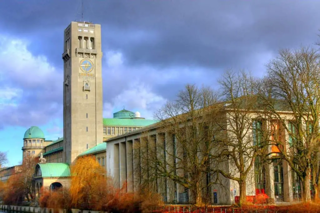 The Deutsches Museum in Munich, Germany, with its grand architectural design, a towering clock, and distinctive green rooftops under a dramatic sky. As the world’s largest museum dedicated to science and technology, it is a fascinating destination for curious minds and one of the top educational experiences in "Things to do in Munich."