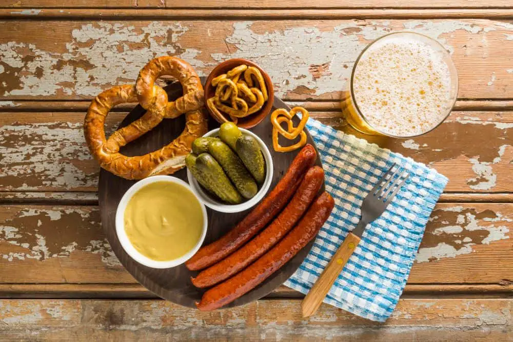 A traditional Bavarian meal featuring sausages, pretzels, mustard, pickles, and beer on a rustic wooden table. A delicious experience to enjoy during a Munich Itinerary 3 Days.