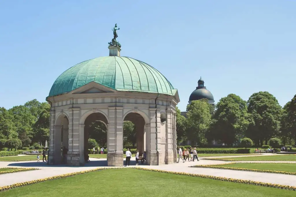 The Hofgarten in Munich, Germany, featuring the elegant Diana Temple with its green copper dome, surrounded by manicured lawns and colorful flowers on a bright summer day. A peaceful retreat in the heart of the city, this historic garden is a must-visit when exploring "Things to do in Munich."