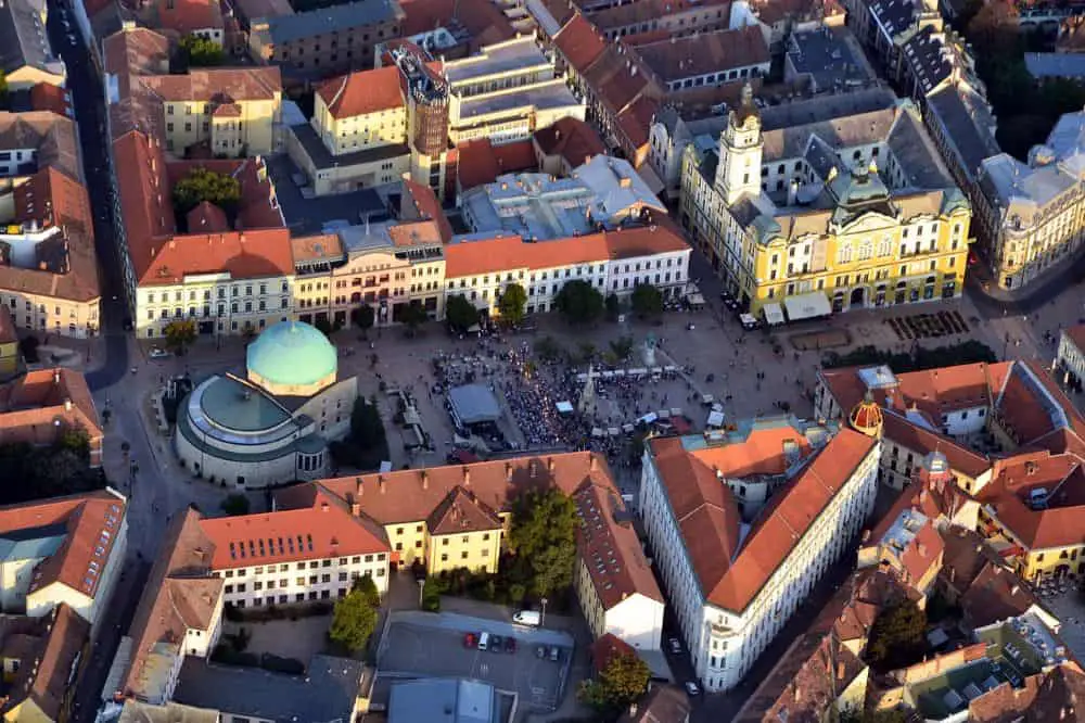  An aerial view of Pécs' central square, showcasing historic architecture, the Pasha Qasim Mosque, and a lively crowd. A charming and affordable city, perfect for Cheap Travel Destinations in Europe Summer.