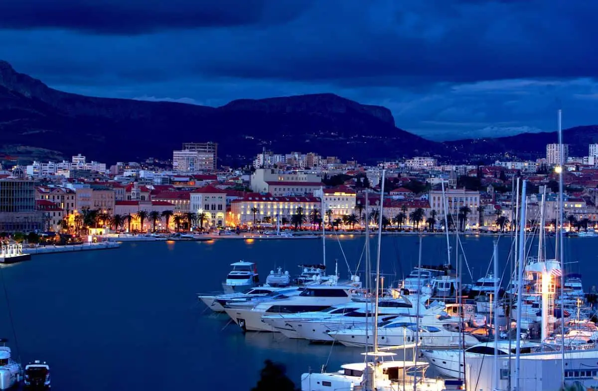 A stunning night view of Split's marina with luxurious yachts docked along the illuminated waterfront, backed by the city's historic architecture and mountains. This breathtaking coastal city is an ideal choice for Cheap Travel Destinations in Europe Summer, offering affordable seaside charm and rich cultural heritage.